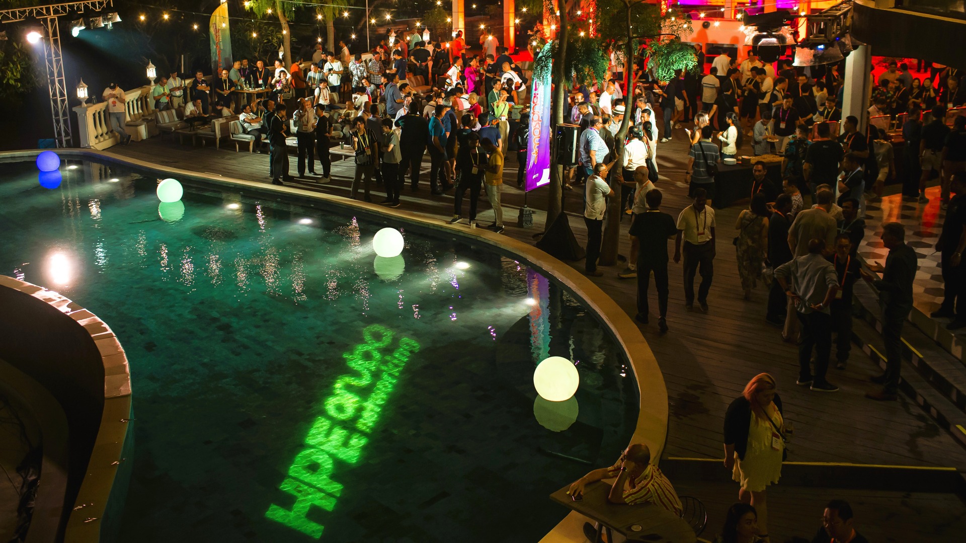 Atmosphere '23 attendees at a nighttime pool party, surrounded by colorful lights and a festive atmosphere.